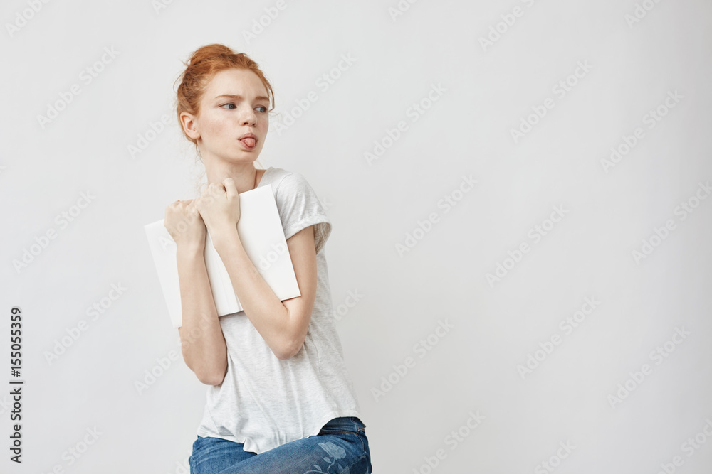 Scared beautiful redhead girl holding book showing tongue. Scared beautiful redhead girl holding book showing tongue.