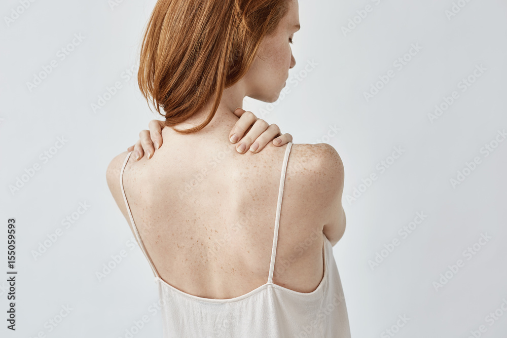 Young redhead girl with freckles posing back to camera.