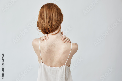 Young redhead girl with freckles posing back to camera.