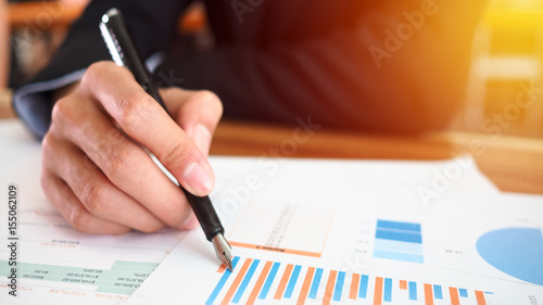 Business man hand holding pen working with graph plans blurred focus for business background