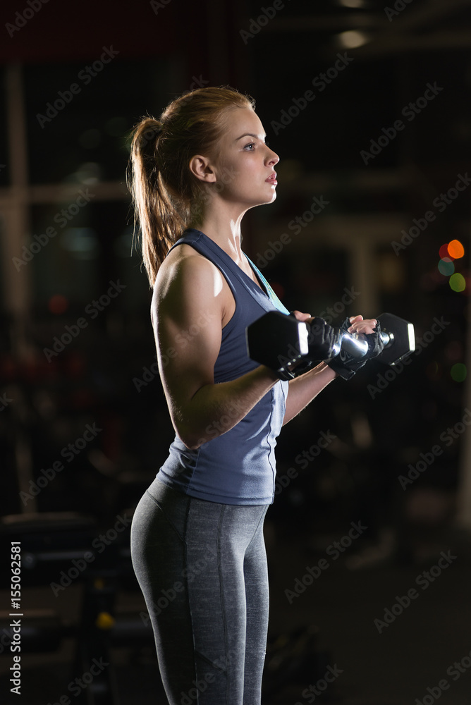 Beautiful sporty woman doing power fitness exercise at sport gym. Girl with dumbbell on black.