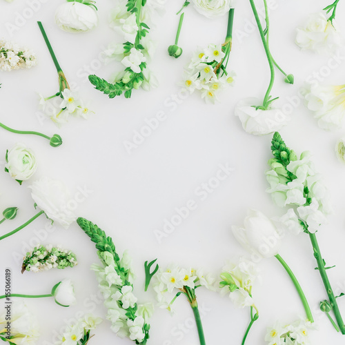 Round frame of spring flowers - ranunculus, snapdragon and tulip on white background. Flat lay, top view.