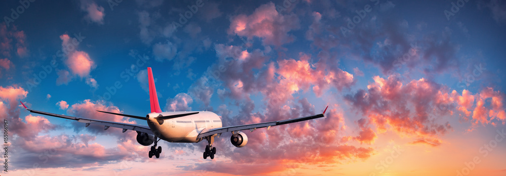 Naklejka premium Samolot. Krajobraz z dużym białym pasażerskim samolotem lata w niebieskim niebie z czerwonymi i pomarańczowymi chmurami przy kolorowym zmierzchem. Podróżować. Samolot pasażerski. Podróż służbowa. Samolot komercyjny. Samolot