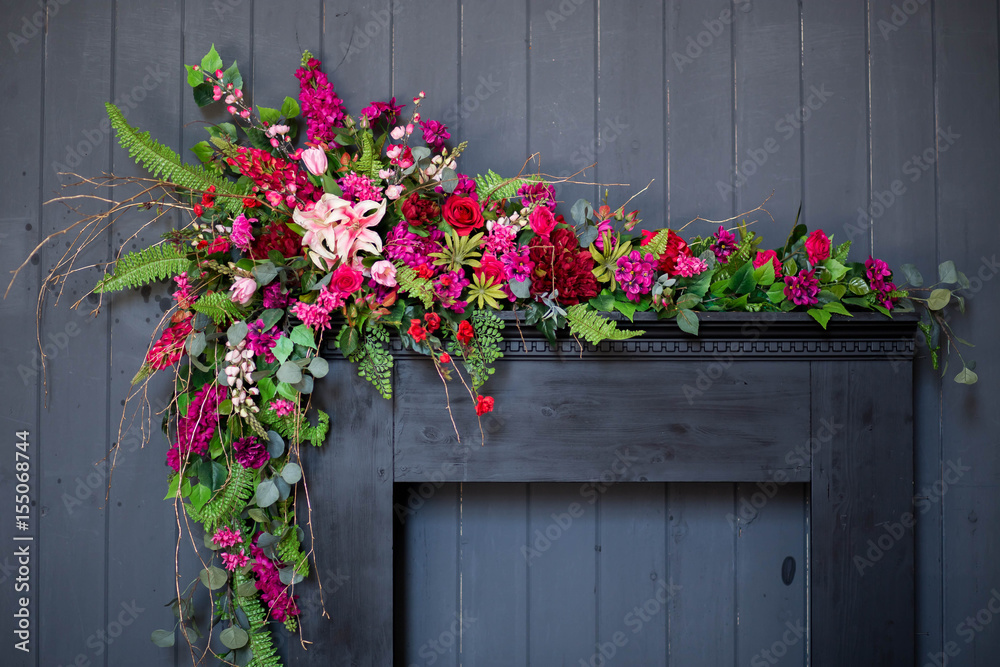 Fototapeta premium beautiful scenery in the Studio gray background fireplace bright red flowers with greenery, bottle Golden silvery candle