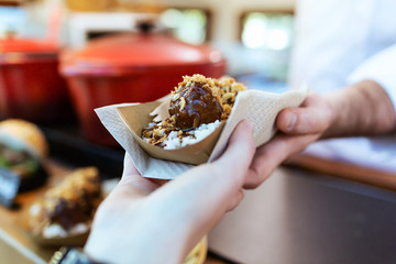 Hand of a girl picking up the meatballs she has bought in a food truck.