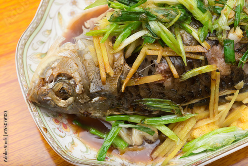 fresh steamed whole fish covered with herbs onions and sauce close up
