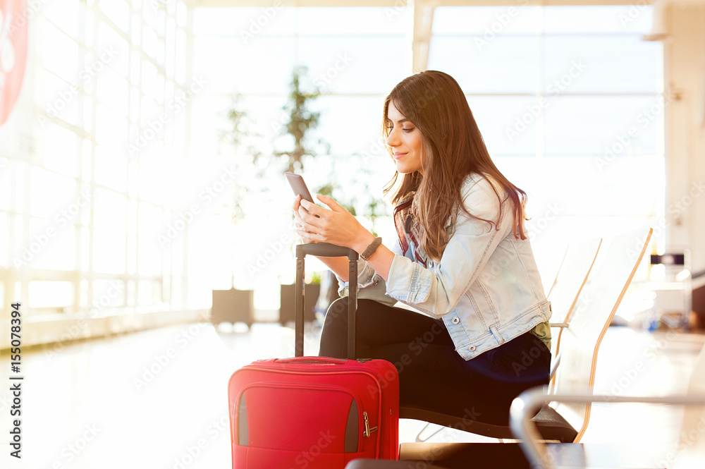 Casual young woman sitting, using her cell phone while waiting to board a plane at the airport terminal waiting room. Casual young woman sitting, using her cell phone while waiting to board a plane at the airport terminal waiting room.