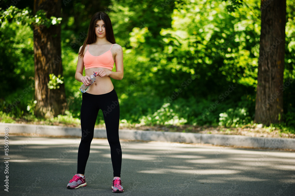 Fitness sport girl in sportswear posed at road in park with bottle of water, outdoor sports, urban style.