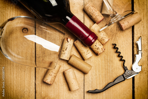 Botella de Vino tinto junto a una copa de cristal, corchos y descorchador sobre una mesa de madera rústica. Vista superior y de cerca photo