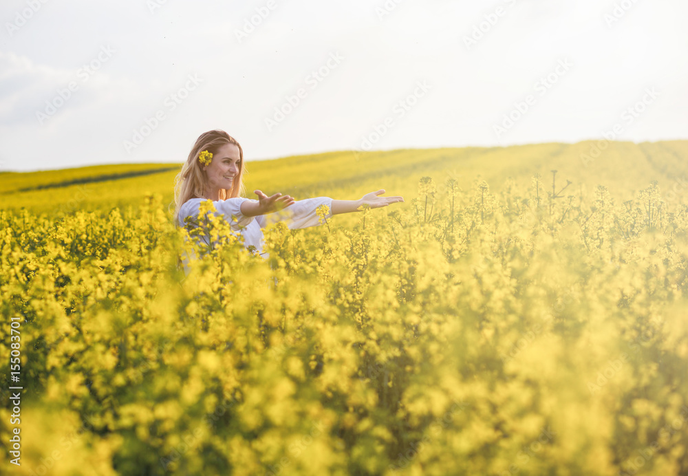Fototapeta premium Smiling woman in yellow rapeseed field at sunny day