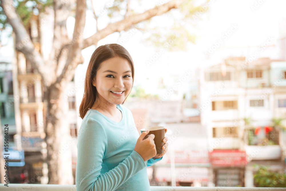 Portrait of a happy asian woman thinking and holding coffee or tea cup at breakfast