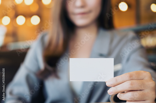 A beautiful Asian business woman holding and showing empty business card in modern loft cafe