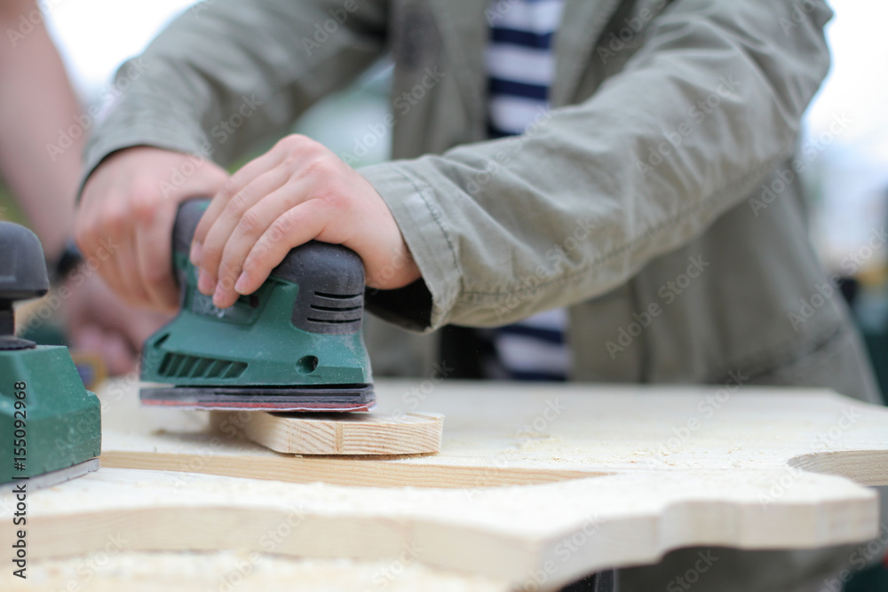 Closeup photo of diy father teaching son tinkering, using jig saw. Classes for young carpenter pollish wood board form using jigsaw. Toy making. Dreaming of future profession. child woodcarving lesson Closeup photo of diy father teaching son tinkering, using jig saw. Classes for young carpenter pollish wood board form using jigsaw. Toy making. Dreaming of future profession. child woodcarving lesson