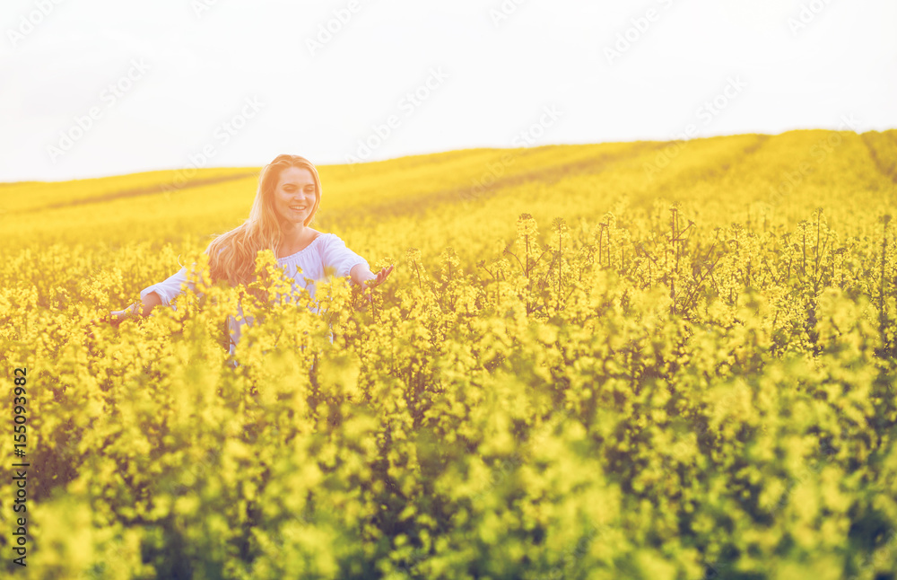 Fototapeta premium Smiling woman walking in yellow rapeseed field at sunset