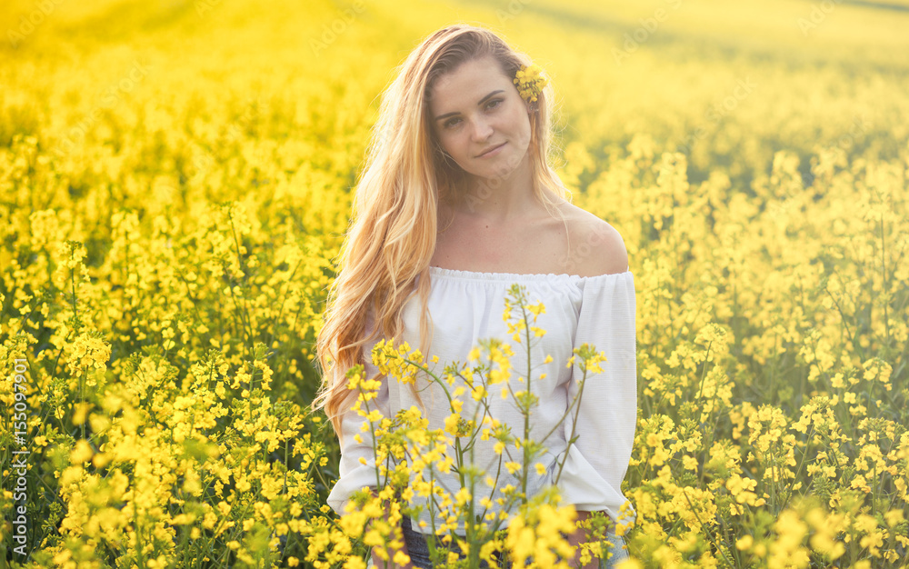 Smiling woman in yellow rapeseed field at sunny day