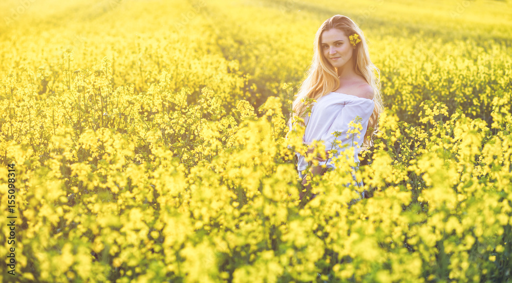 Smiling woman in yellow rapeseed field at sunny day