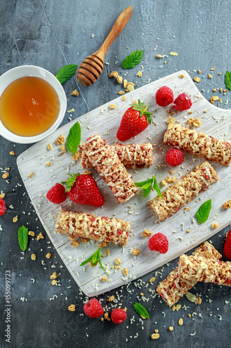 Granola bar with strawberries, raspberry honey and white chocolate on cutting board