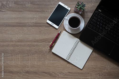 Note books, pens, coffee, mobile phones and laptop are placed on table wooden and have space for text input. copy space