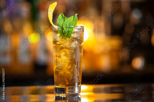 Photography Closeup glass of cuba libre cocktail decorated with mint at orange lighted bar counter background