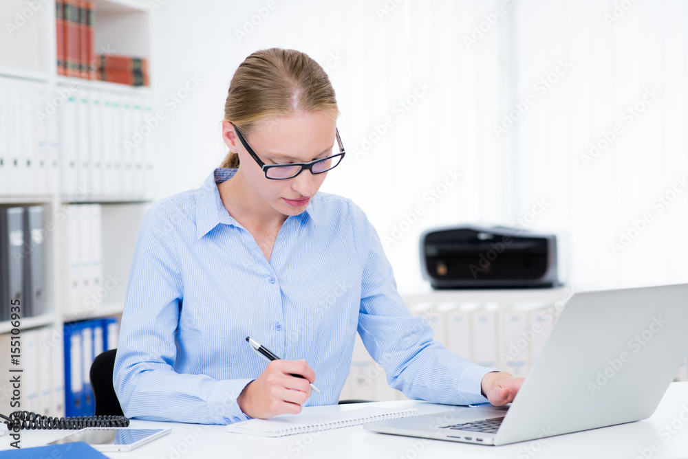 mitarbeiterin sitzt mit notebook am schreibtisch mitarbeiterin sitzt mit notebook am schreibtisch