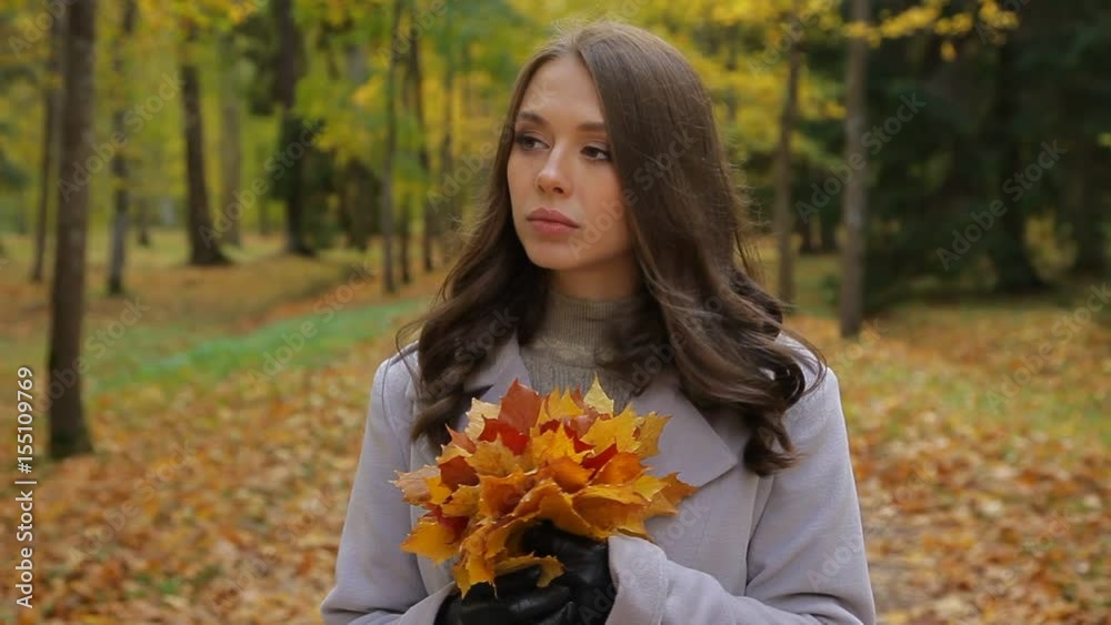 Young woman in love, with a bunch of yellow leaves, looks for her honey in a park,