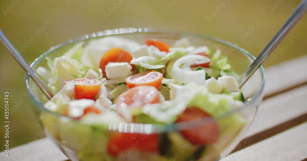Bowl of fresh mixed green salad with lettuce  leafy greens and tomato served outdoors in summer as an accompaniment to a barbecue