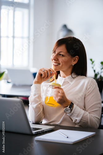 Smiling elegant businesswoman in bright office drinking orange juice