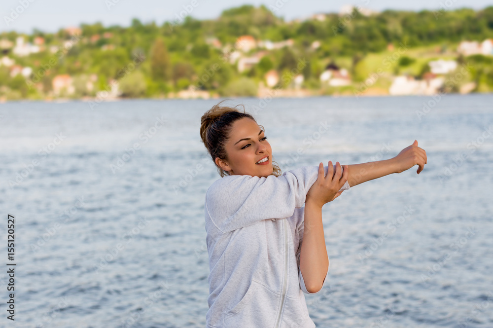 Beautiful young woman doing stretching exercises while standing outdoors Beautiful young woman doing stretching exercises while standing outdoors