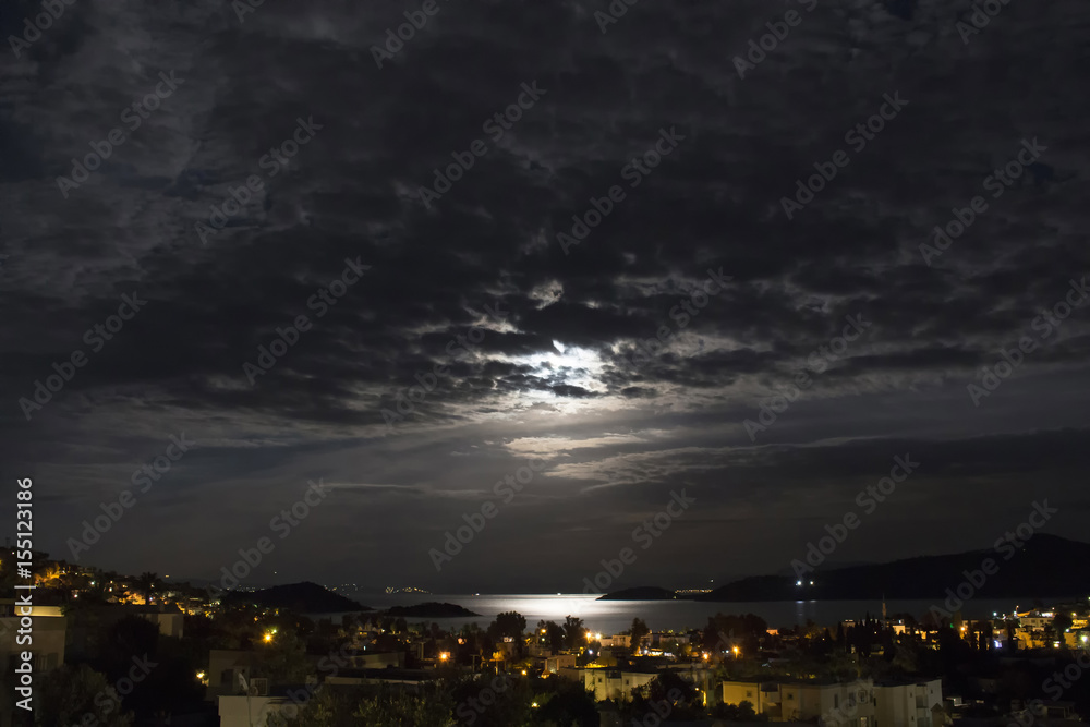 Long exposure of full moon in 2016 summer behind clouds over Aegean sea at Turkbuku village in Bodrum peninsula. Light shines on sea surface.