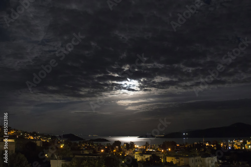 Long exposure of full moon in 2016 summer behind clouds over Aegean sea at Turkbuku village in Bodrum peninsula. Light shines on sea surface.