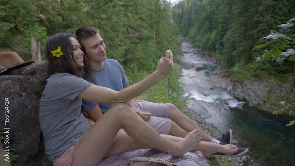 Adventurous Couple Take Selfies Together On A Cliff, Overlooking A River Adventurous Couple Take Selfies Together On A Cliff, Overlooking A River