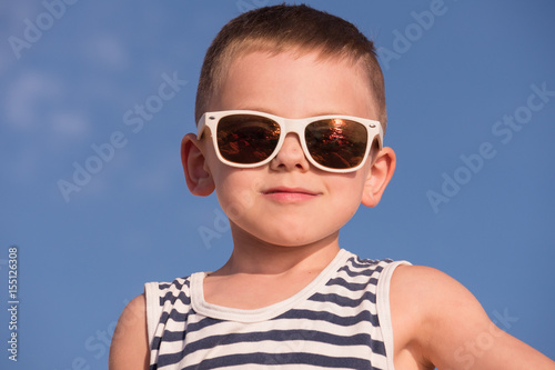 cool smiling little boy wearing sunglasses with ocean sunset reflection