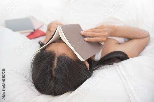 Relaxed Asian girl sleeping on her bed with a book on her face. © eggeeggjiew