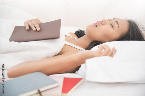 Relaxed Asian girl sleeping with a book on her bed.