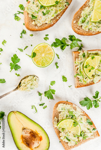 Homemade sandwich toasts with with guacamole, lime lemon and parsley on white table, copy space top view