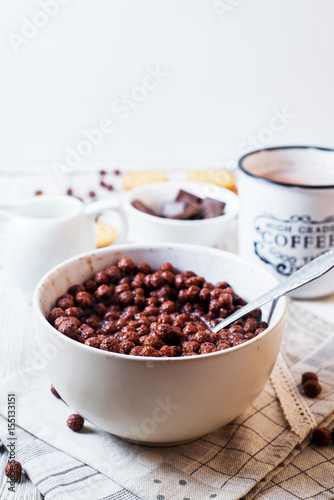 Hearty and tasty breakfast for children, cornflakes, chocolate balls with milk, cocoa and biscuits on a light wooden background 