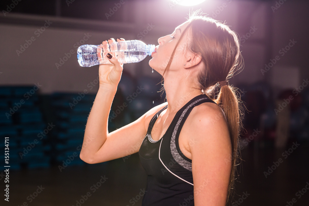 Fitness woman drinking water from bottle. Muscular young female at gym taking a break from workout. Fitness woman drinking water from bottle. Muscular young female at gym taking a break from workout.