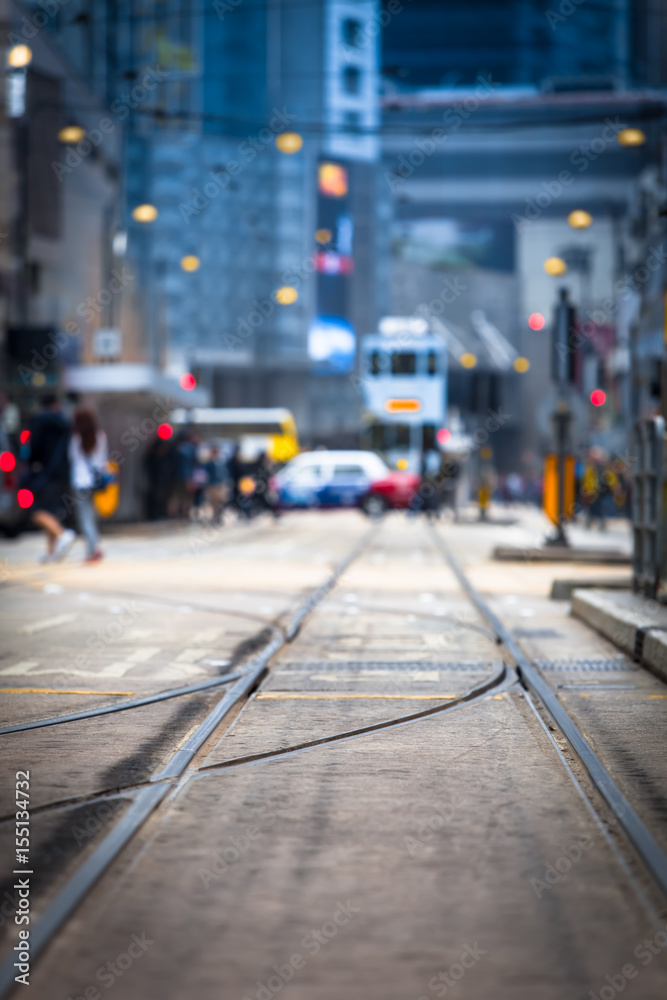 Fototapeta premium Hongkong Street View / tory tramwajowe w kierunku rozmytego tła ruchu miejskiego z tramwajem, samochodem, nierozpoznawalnymi ludźmi i budynkami miejskimi w nocy (miejsce na kopię)