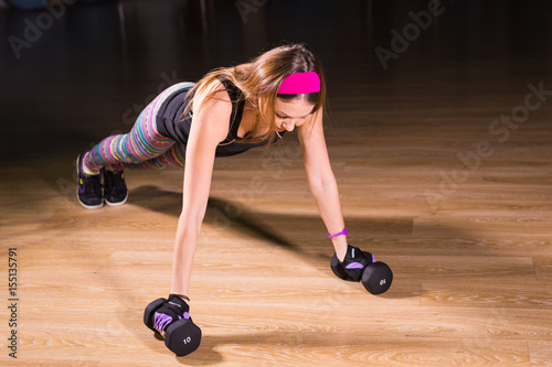 Strong young woman doing push ups exercise with dumbbells. Fitness model doing intense training in the gym.