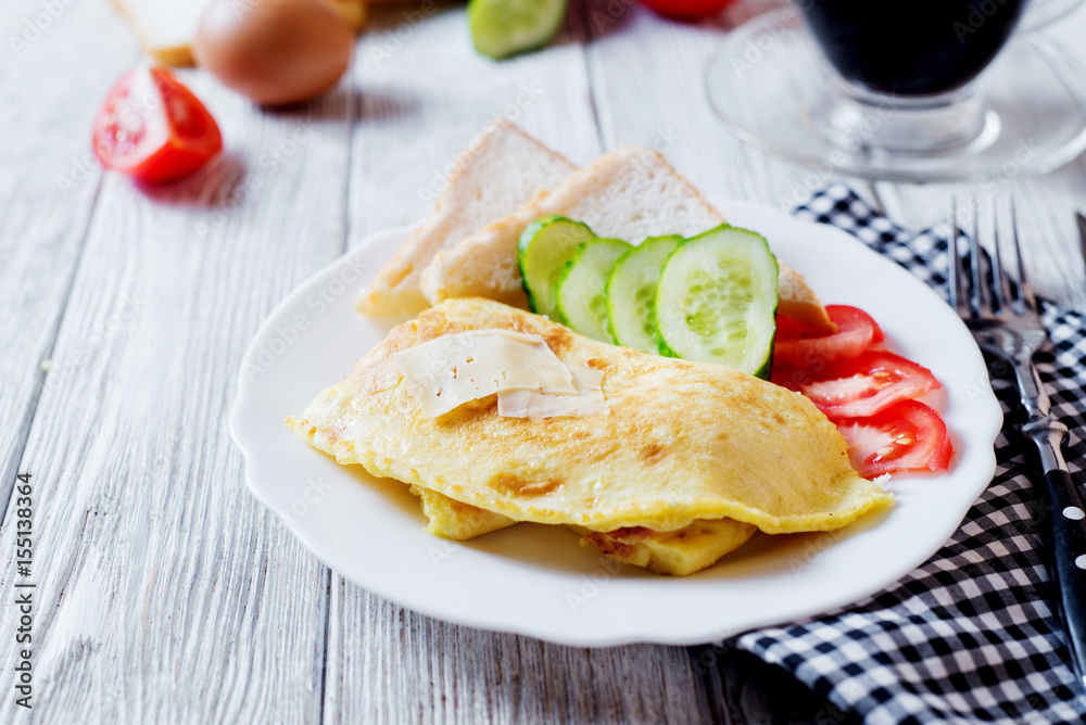 Hearty and tasty breakfast, traditional in the hotel, omelette from chicken eggs with cheese, fresh vegetables - cucumber and tomato, white toast and black coffee on a light wooden background Hearty and tasty breakfast, traditional in the hotel, omelette from chicken eggs with cheese, fresh vegetables - cucumber and tomato, white toast and black coffee on a light wooden background