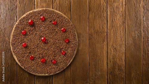 Sweet raw pizza with chocolate and cherry on wooden background