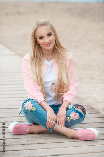 Beautiful autumn woman wear pink jacket posing near the seaa outdoors. Beauty happy long hairl blonde girl smiling at beach. Autumn  style fashion model photo