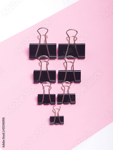 black paper clips on light pink and white background. top view. flat lay. 