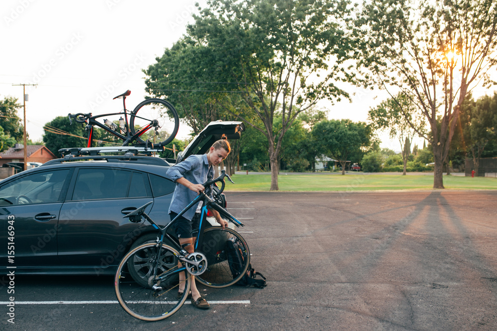 Young sporty and handsome man cyclist assembles his carbon road bike next to the hunchback car with rack Young sporty and handsome man cyclist assembles his carbon road bike next to the hunchback car with rack