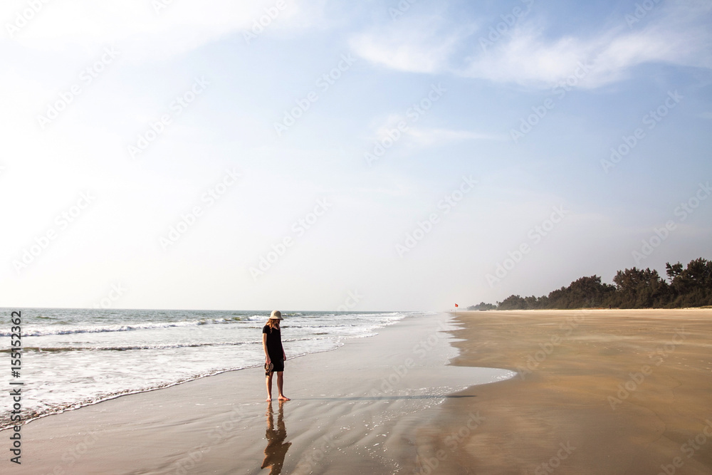 girl in black dress walking on a sand beach