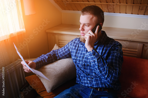 Discussing that document. Serious mature man holding paper and talking on the mobile phone while sitting on the couch at home photo