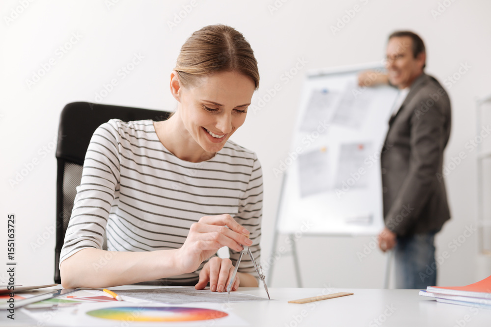 Cheerful female engineer drawing with compasses