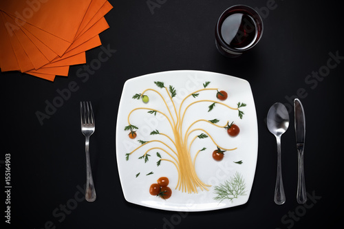Composizione con elementi del tipo pasta, piatto, posate, tovaglioli  e bicchiere posizionati artisticamente su tavolo nero. Sfondo con spazi liberi per testo. photo