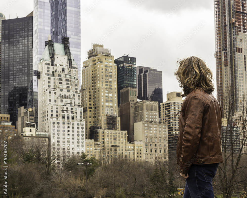 Naklejka premium Long-haired Male In A Leather Jacket Looking At Manhattan Skyscrapers