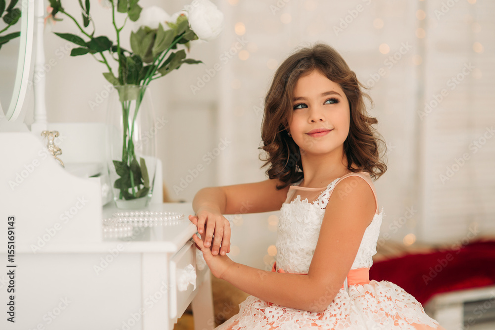 Little beautiful girl with brown hair in a Peach-colored dress. Poses for a photographer